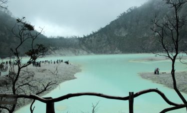 ourists exploring the misty turquoise crater lake surrounded by hills and volcanic terrain at Kawah Putih Bandung, a stunning natural attraction in West Java, Indonesia.