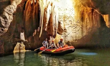 ourists exploring Jomblang Cave on a rafting adventure, surrounded by stunning rock formations and illuminated cave walls in Yogyakarta, Indonesia.