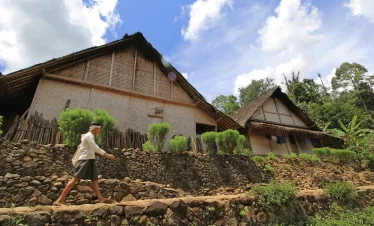 A local man walking barefoot along a stone path in Baduy Village, surrounded by traditional bamboo houses and lush greenery, captured during a Baduy Village exploration in Indonesia.