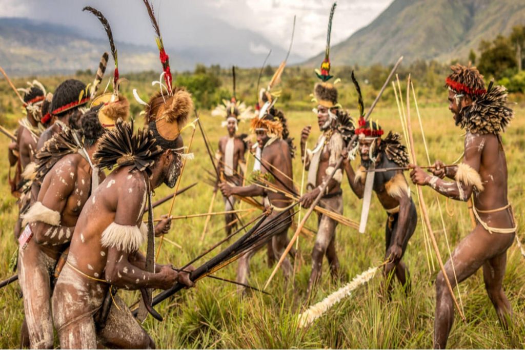 Tribal warriors performing a traditional mock battle with bows and arrows during the Baliem Valley Festival 2026, showcasing the rich cultural heritage of Papua in a scenic highland setting.