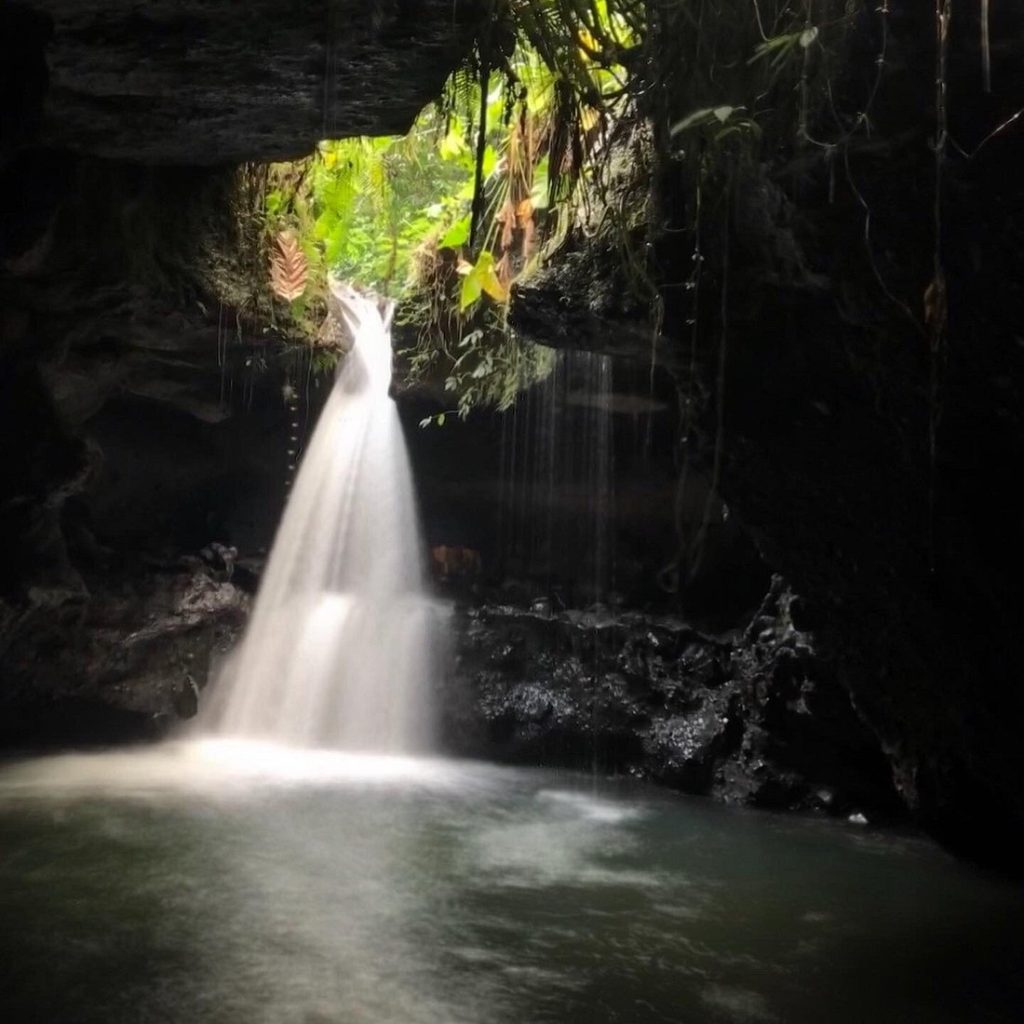 A secluded waterfall flowing into a tranquil pool inside a rocky cave, highlighting one of the hidden waterfalls in Lombok surrounded by lush tropical vegetation.