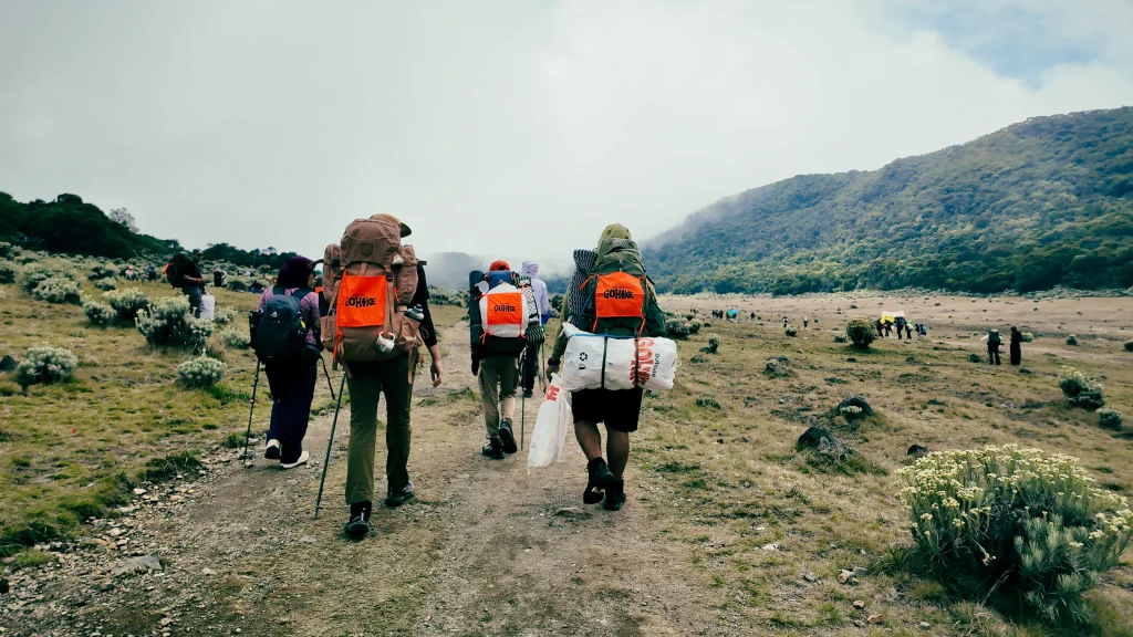 Group of hikers walking across a scenic mountain trail during trekking in Indonesia, surrounded by open grasslands and lush volcanic landscapes
