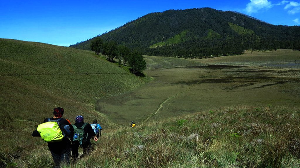 Group of hikers descending a vast green valley and mountain landscape during an adventurous trekking in Indonesia experience.