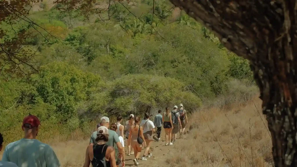 Group of hikers walking along a scenic trail through dry hills and lush greenery, showcasing an authentic trekking in Indonesia experience.